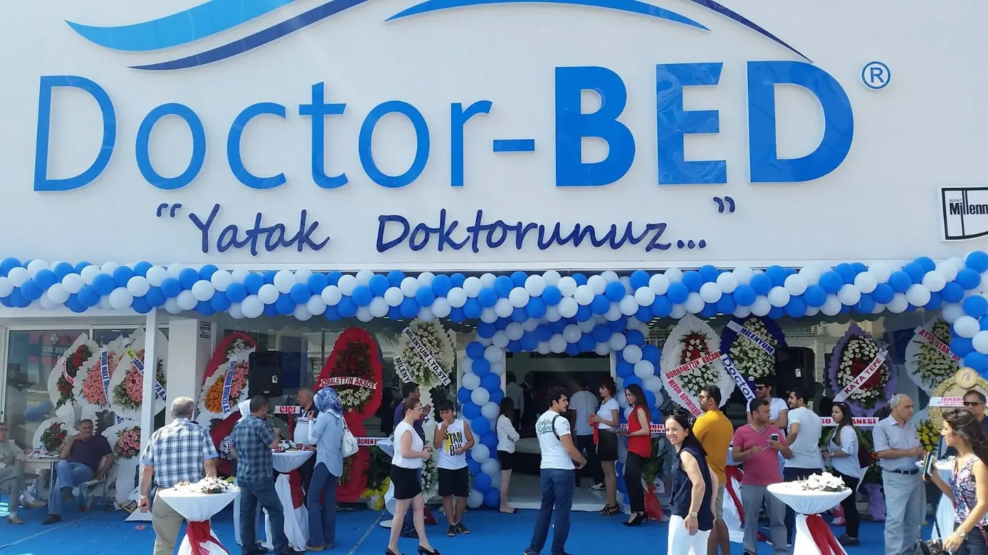 Açılış günü mağaza girişinde mavi-beyaz balon süsleme, çelenk sırası ve davetli kalabalığı.