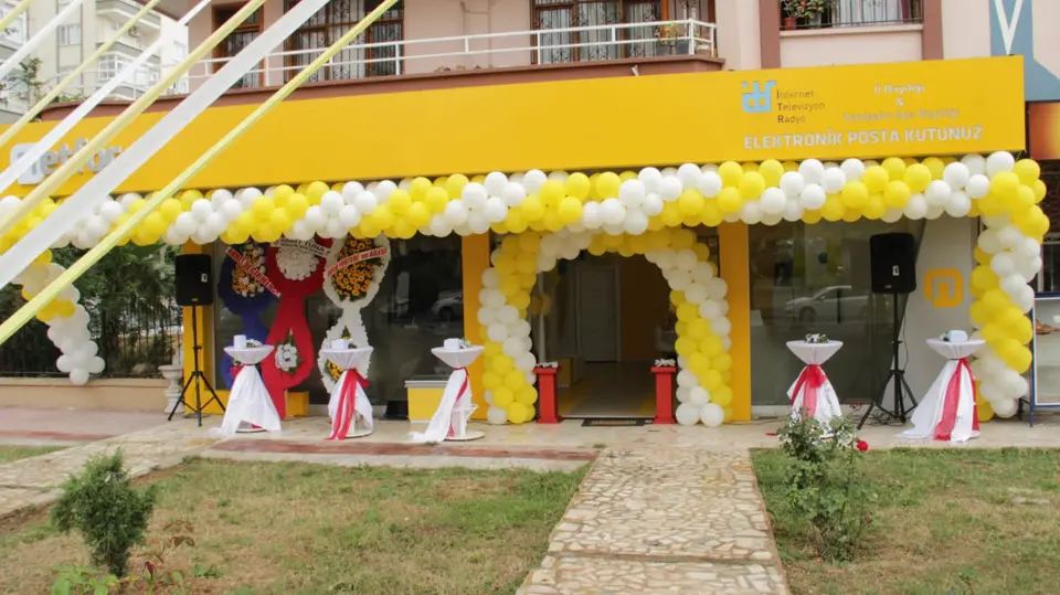 Bina girişinde sarı-beyaz balon kemeri, çiçek panoları ve karşılama düzeni.